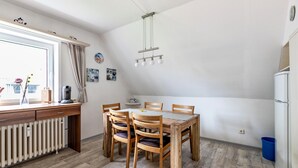 Un coin repas avec une table et des chaises en bois, une fenêtre avec des rideaux, un radiateur et un luminaire suspendu.