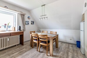Ein Essbereich mit Holztisch und Stühlen, einem Fenster mit Vorhängen, einem Heizkörper und einer Pendelleuchte.