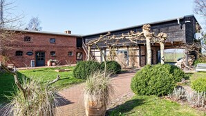 A brick building with a modern extension, a paved pathway, and various plants.