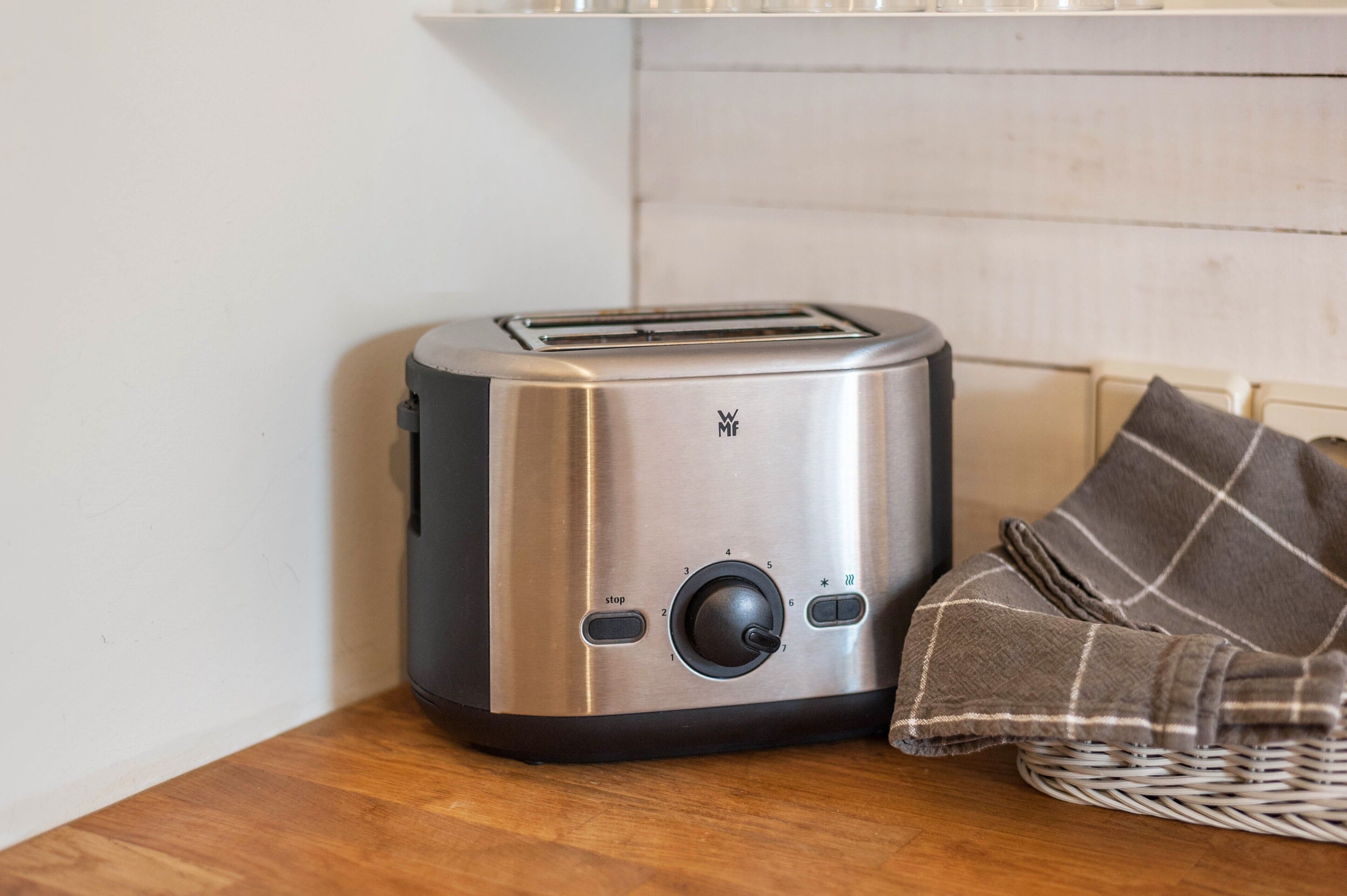 A toaster on a wooden table with a checkered cloth and a wicker basket.