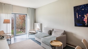 Een moderne woonkamer met een grijze bank, een klein rond tafeltje, een stoel en een groot raam met gordijnen.