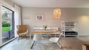 A dining area with a table, chairs, a hanging light fixture, a bookshelf, and a window with curtains. - Holiday Apartment DREI at Hof Himmelgrün with Large Garden (Saal)