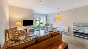 A modern living room with a sofa, a television, a dining table, and a bookshelf. - Holiday Apartment DREI at Hof Himmelgrün with Large Garden (Saal)