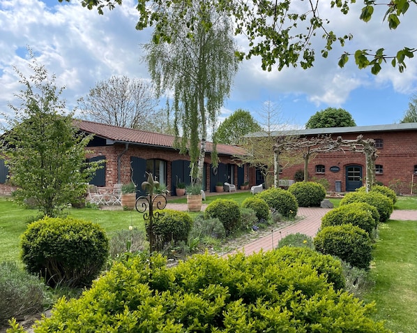 A brick building with a red-tiled roof, surrounded by well-maintained gardens and a clear sky.
