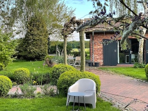 A garden with a paved path, a white plastic chair, and a brick building with a door.