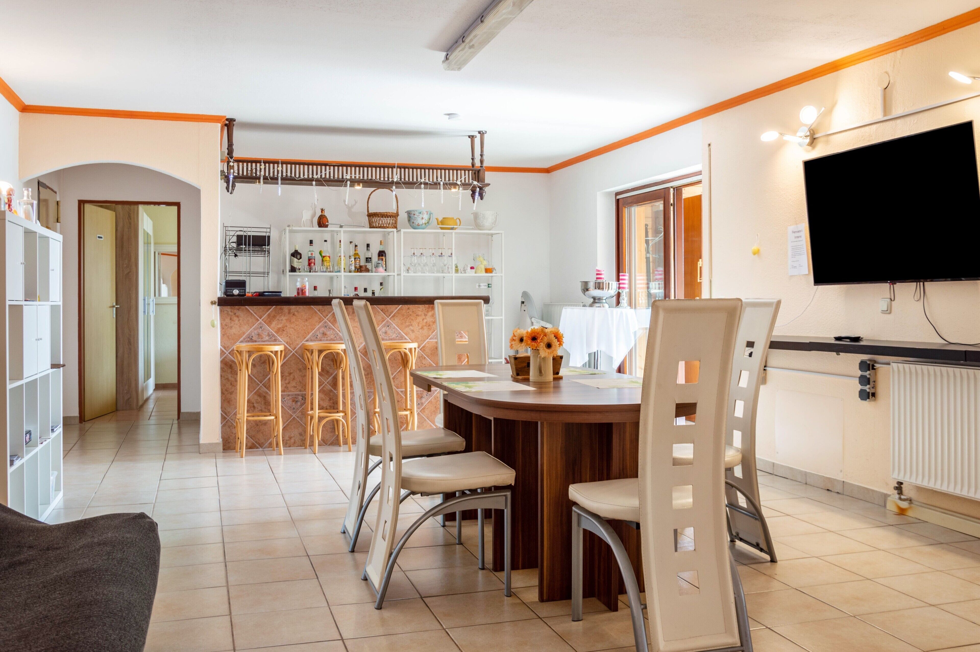 A modern kitchen with a dining area, bar stools, and a TV.