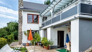Ein zweistöckiges Haus mit Balkon, Sitzgelegenheit im Freien und Kübelpflanzen.