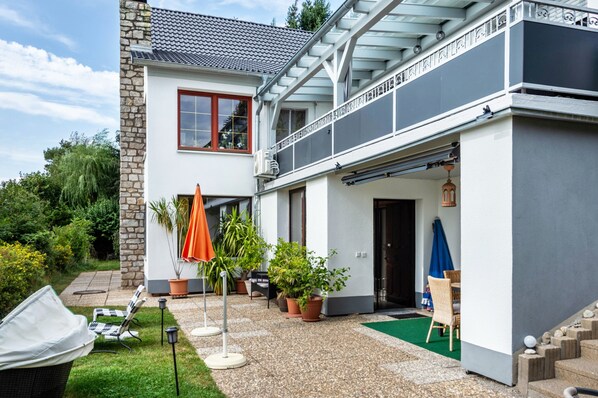 A two-story house with a balcony, outdoor seating area, and potted plants.