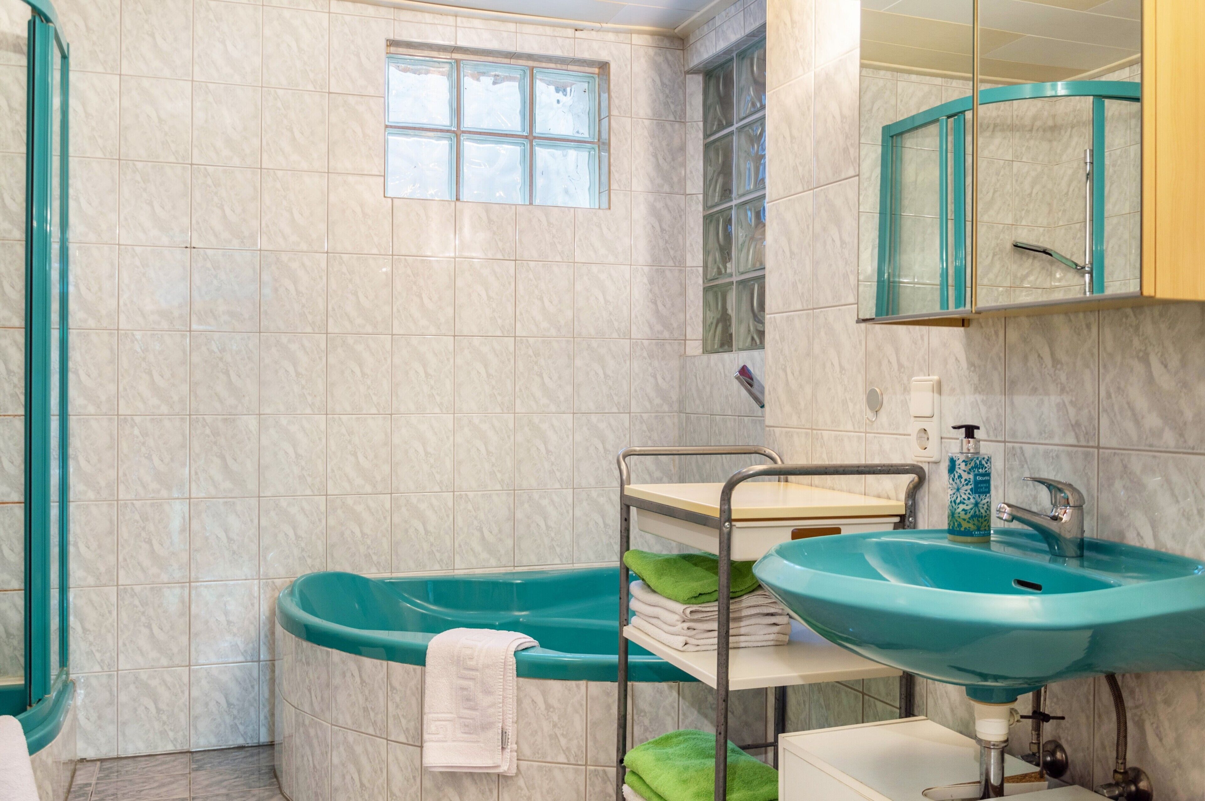 A bathroom with a bathtub, a sink, a mirror, and a window.