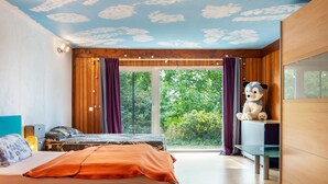Ein Schlafzimmer mit Bett, Schreibtisch, einem großen Fenster mit Vorhängen und einer Decke mit Wolkenmuster.