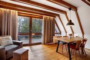 A room with a wooden ceiling, a dining table with chairs, a sofa, and a window with curtains.