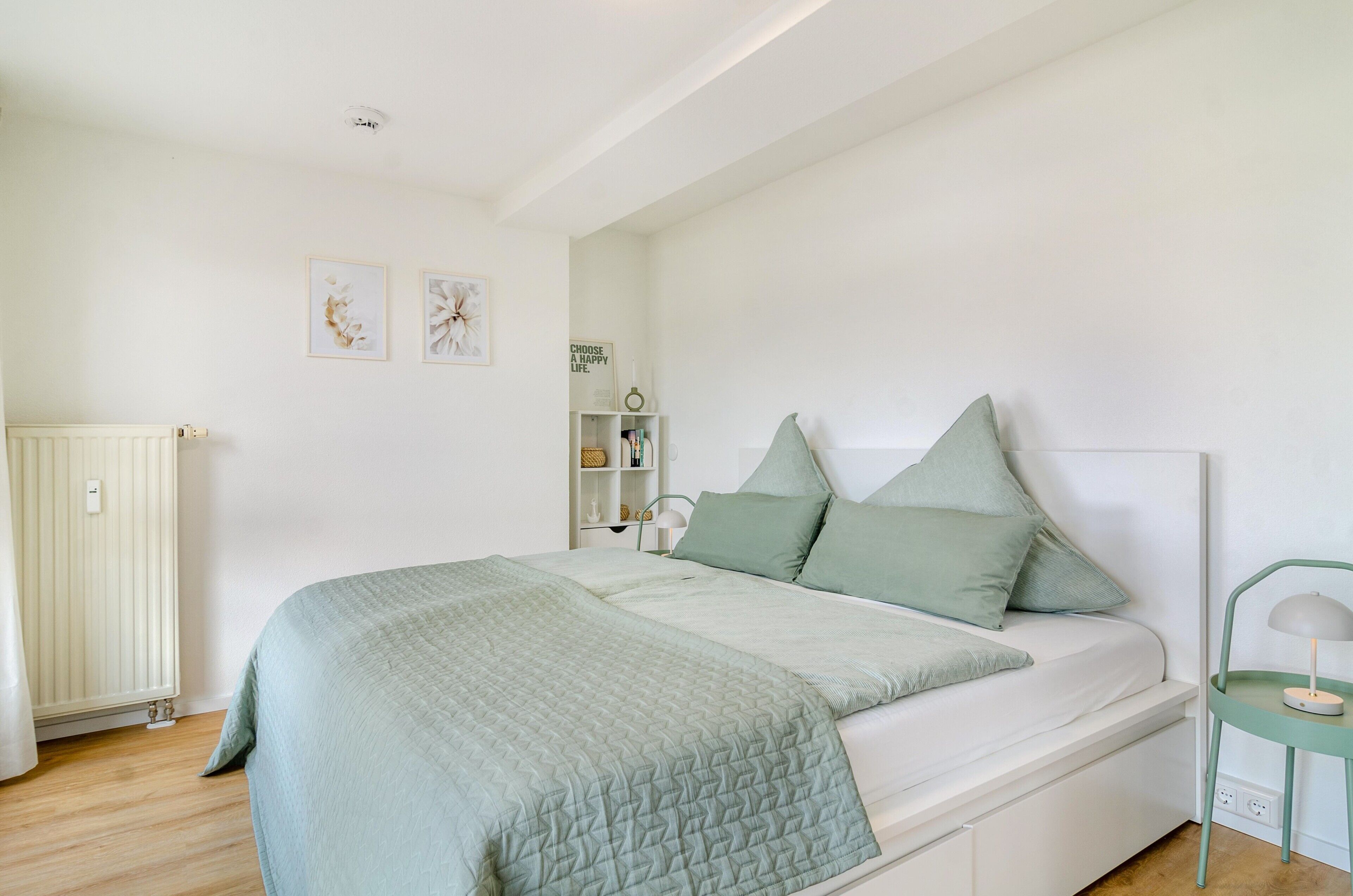 A bedroom with a bed, bedside table, lamp, and wall art.