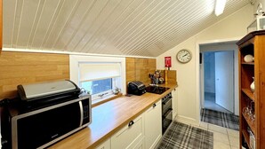 A compact kitchen with a microwave, toaster, and sink. There is a clock on the wall and a plaid rug on the floor. - Ameliafield Cottage in Prestwick (Prestwick)