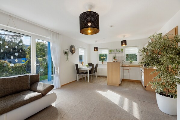 A modern kitchen with a dining area, large windows, and a potted plant.