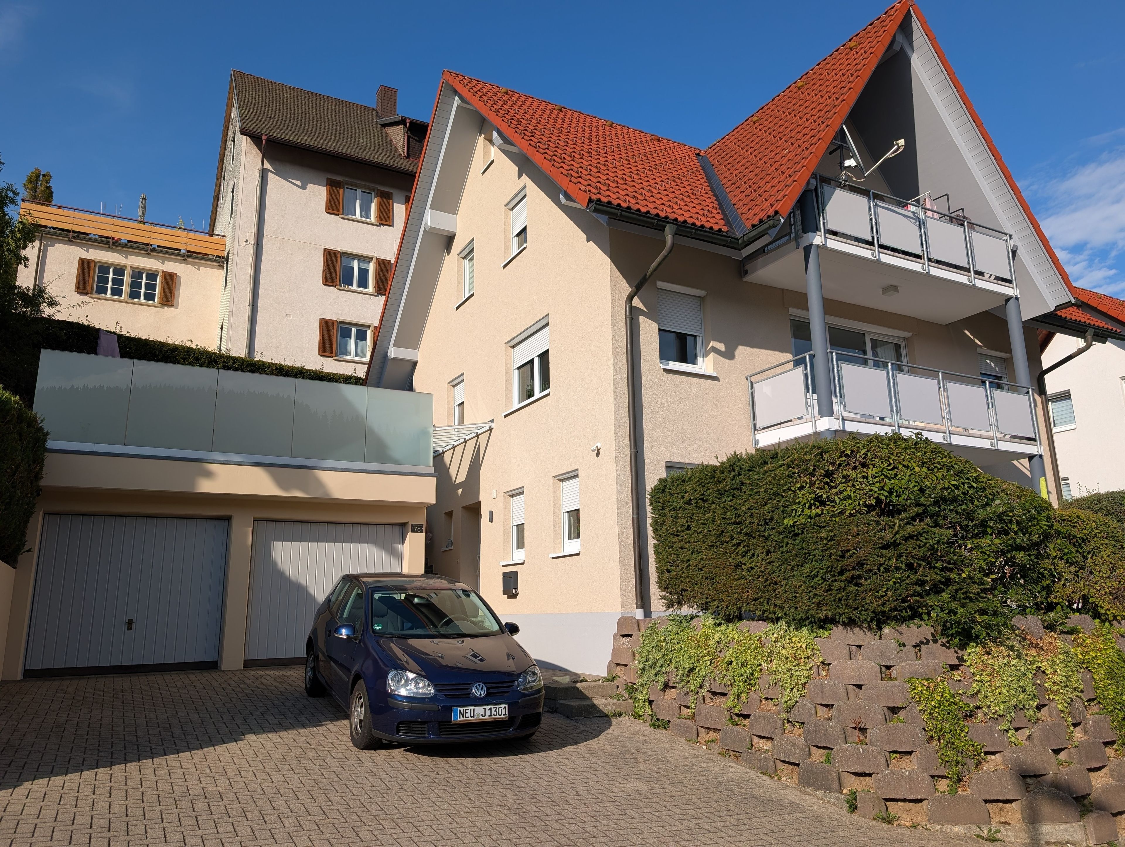 A residential building with a car parked in the driveway, a gated garage, and a well-maintained hedge.