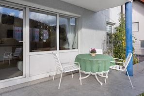 A patio with a table and two chairs, a green tablecloth, and a potted plant.