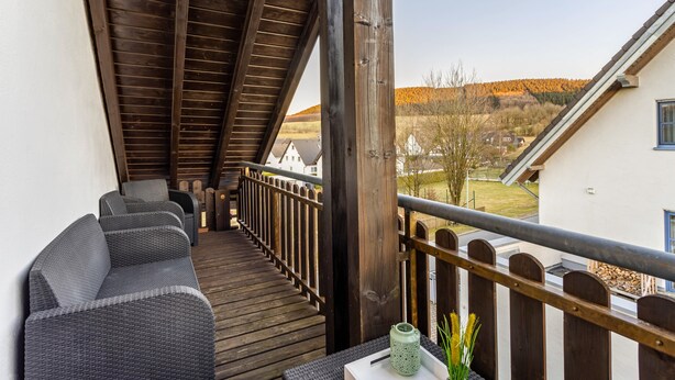 A wooden deck with a sofa and a lantern. - Apartment 'Ferienwohnung Rinke' with Mountain View and Balcony (Schmallenberg)