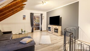 A modern living room with a sofa, a flat-screen TV, a staircase, and a view through a glass door. - Apartment 'Ferienwohnung Rinke' with Mountain View and Balcony (Schmallenberg)
