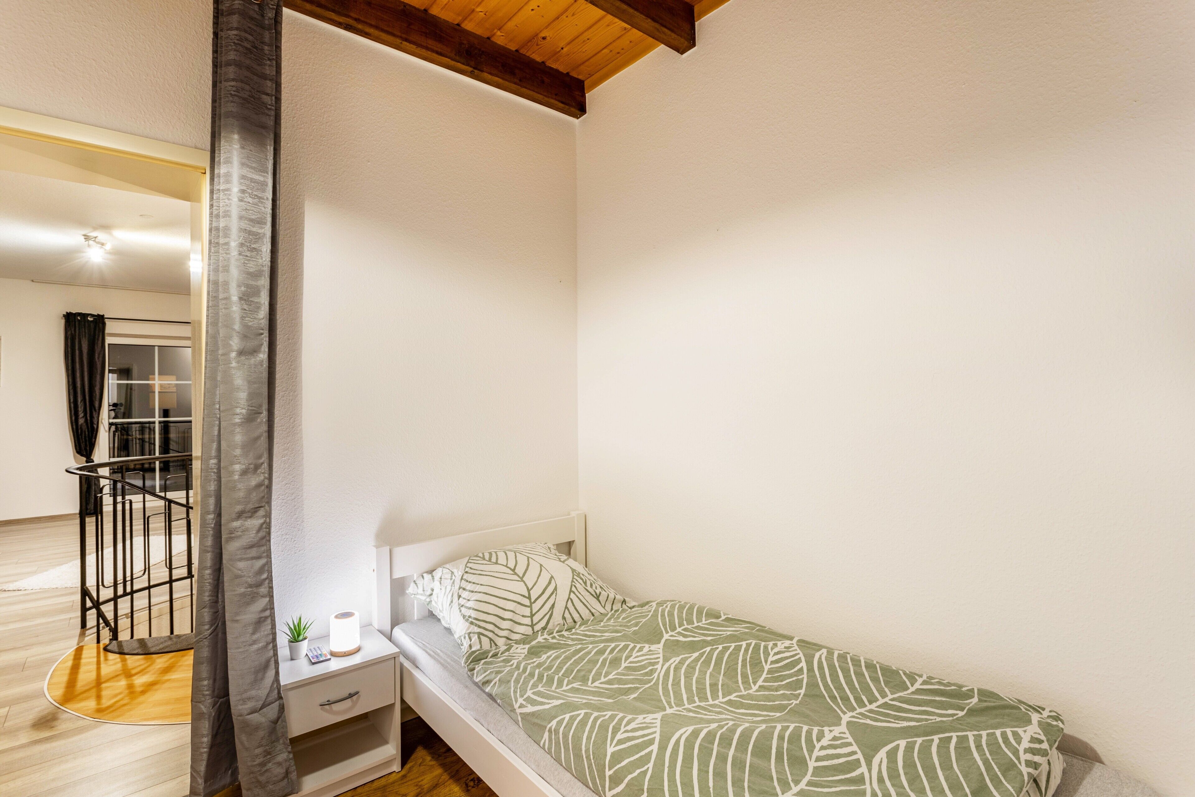 Ein Schlafzimmer mit einem Bett, einem Nachttisch, einer kleinen Pflanze und einem Holzbalken an der Decke.