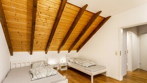 A bedroom with a sloped ceiling, wooden beams, two beds, bedside tables, and a door leading to another room. - Apartment 'Ferienwohnung Rinke' with Mountain View and Balcony (Schmallenberg)