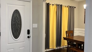 A hallway with a white door, a dining area with a wooden table and chairs, and a set of curtains.