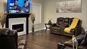 A living room with a fireplace, leather sofas, a TV, and a ceiling fan.