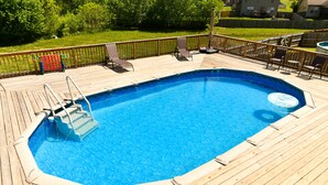 A rectangular swimming pool with a wooden deck, surrounded by a wooden fence and a grassy yard.