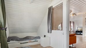 A room with a sloped ceiling, a bed with gray bedding, a small white nightstand, a gray furry rug, and a wooden floor. - "Elara" - 300m from the sea by Interhome (Thyholm)