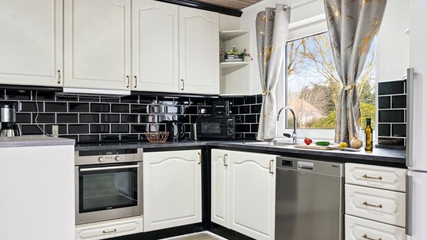 A modern kitchen with white cabinets, black backsplash, stainless steel appliances, and a window with curtains. - "Elara" - 300m from the sea by Interhome (Thyholm)
