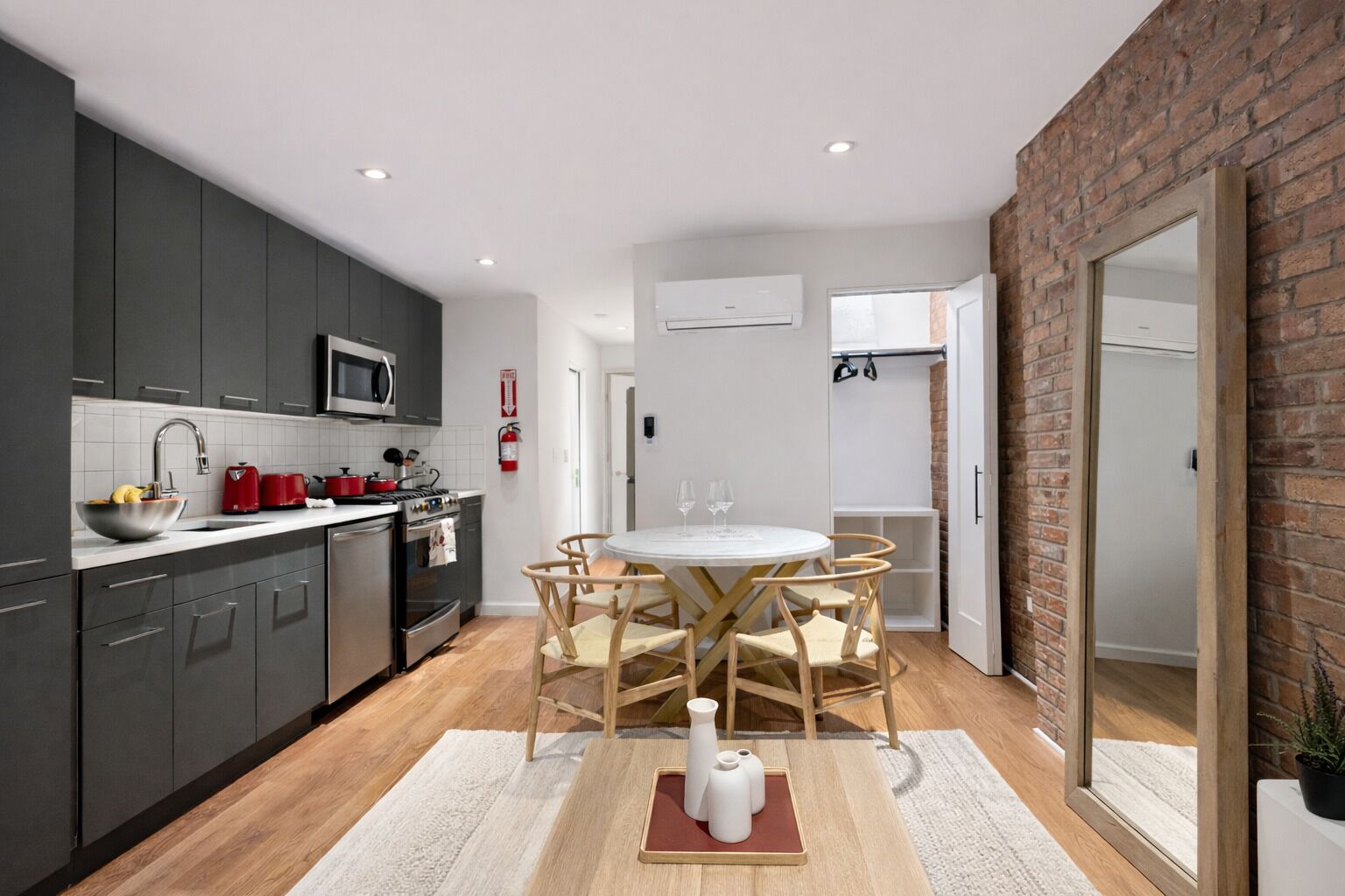 A modern kitchen with dark cabinets, a microwave, and a red kettle. There is a dining area with a round table and chairs.