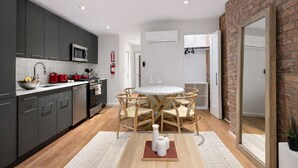 Una cocina moderna con armarios oscuros, un microondas y una tetera roja. Hay una zona de comedor con una mesa redonda y sillas.