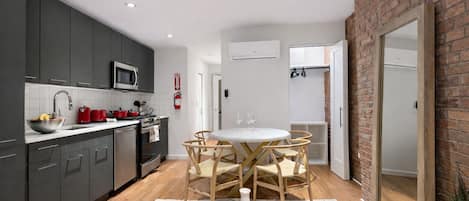 A modern kitchen with dark cabinets, a microwave, and a red kettle. There is a dining area with a round table and chairs.