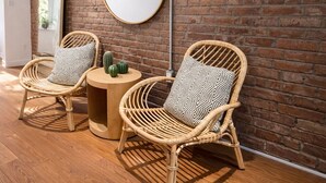 Una habitación con dos sillones de mimbre, una mesa redonda y un espejo grande en una pared de ladrillo.