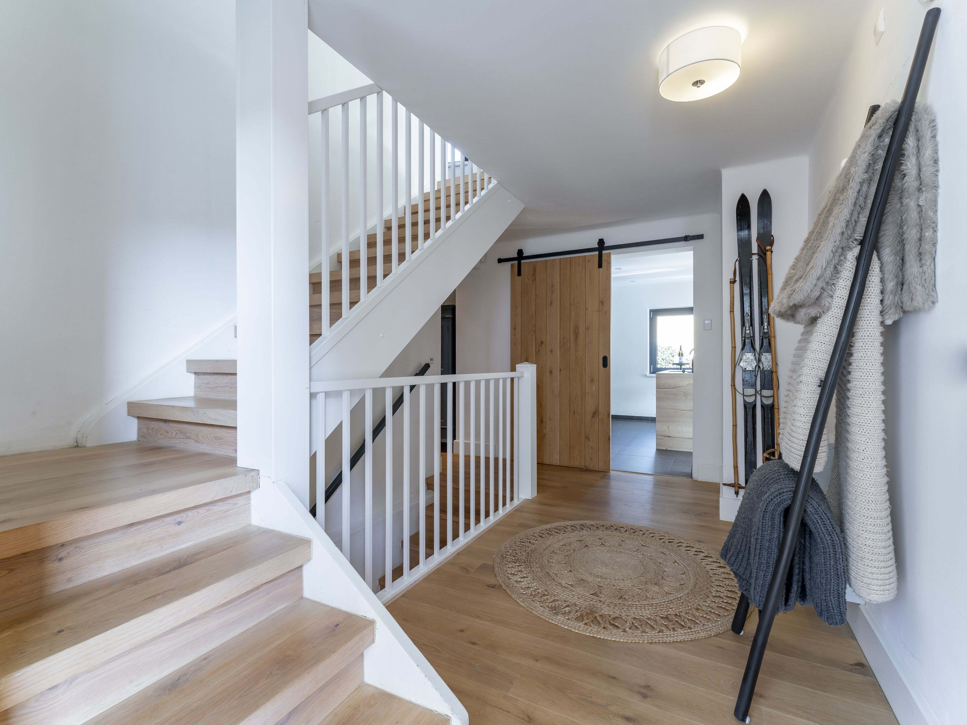 Un escalier avec des marches en bois et une rampe blanche mène à une pièce dotée d’une grande fenêtre.