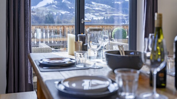 Mesa de jantar com pratos, copos e velas, com vista para uma paisagem montanhosa coberta de neve.