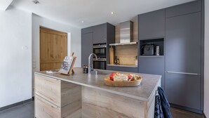Cozinha moderna com ilha central, armários de madeira e eletrodomésticos de aço inoxidável.