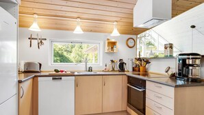 Een moderne keuken met houten kastjes, een ingebouwde oven, een koffiezetapparaat en een raam dat voor natuurlijk licht zorgt.