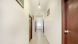 A hallway with a wooden door on the right, a light fixture above, and a door at the end. - iROOMZ Hotel Royal Hill Park (Hyderabad)