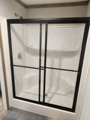 Une douche fermée par des parois en verre, avec un cadre noir, un drain apparent et une pomme de douche.