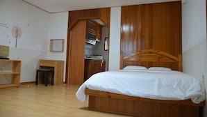 Ein Schlafzimmer mit einem hölzernen Bett, einem kleinen Schreibtisch und einer Küchenzeile im Hintergrund.