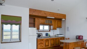 Eine Küche mit Holzausstattung, einem weißen Kühlschrank, einer Mikrowelle, einem Herd und einem Fenster mit Blick ins Grüne.