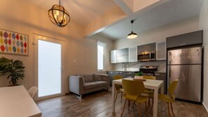A modern kitchen with stainless steel appliances, a dining area with yellow chairs, and a grey sofa. - La Mona Suites 2 Bedroom Family Apartment (San Juan)