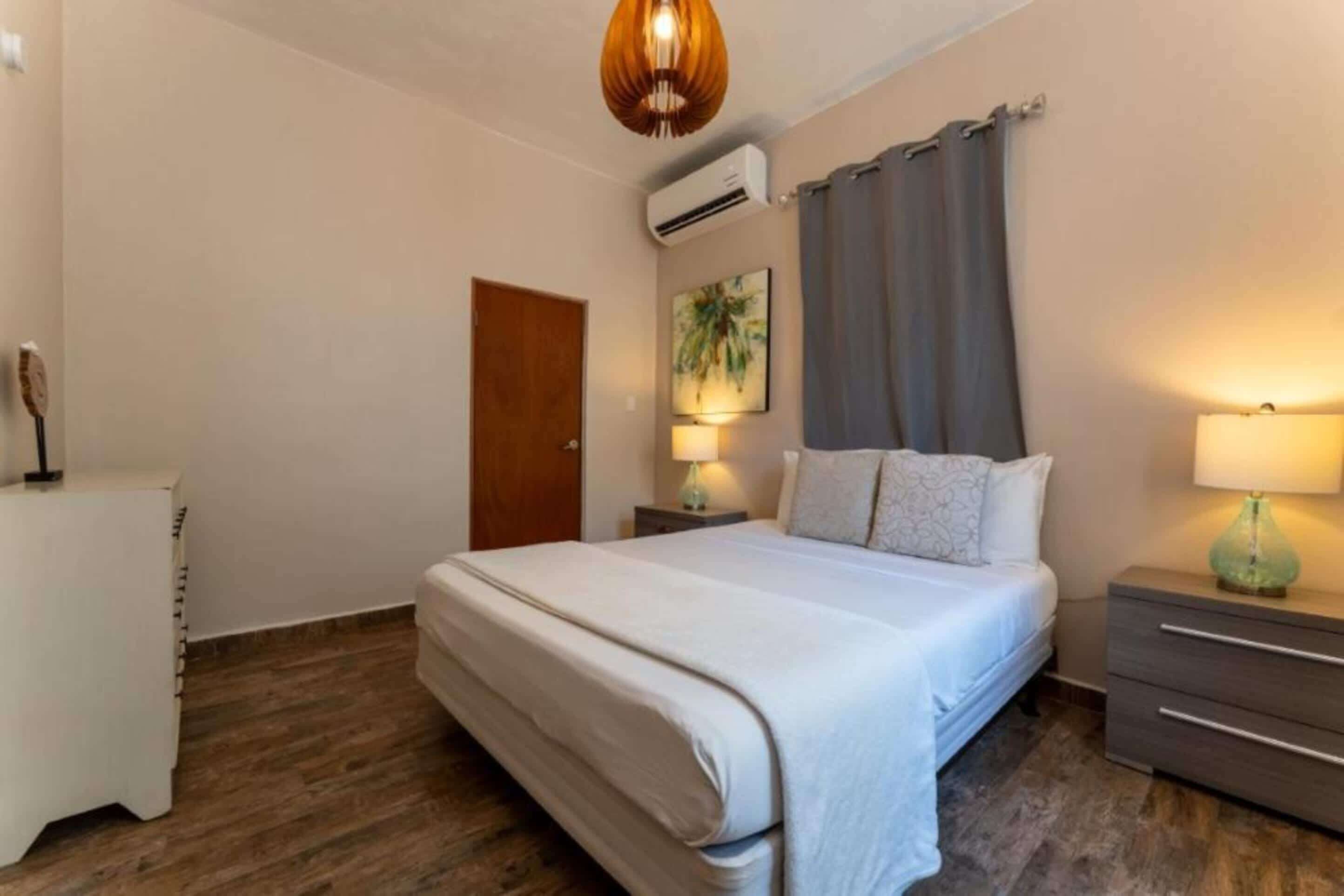 Une chambre à coucher avec un lit, des tables de chevet, une lampe, une porte et un appareil de climatisation.