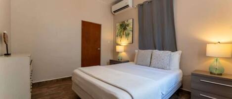 Une chambre à coucher avec un lit, des tables de chevet, une lampe, une porte et un appareil de climatisation.