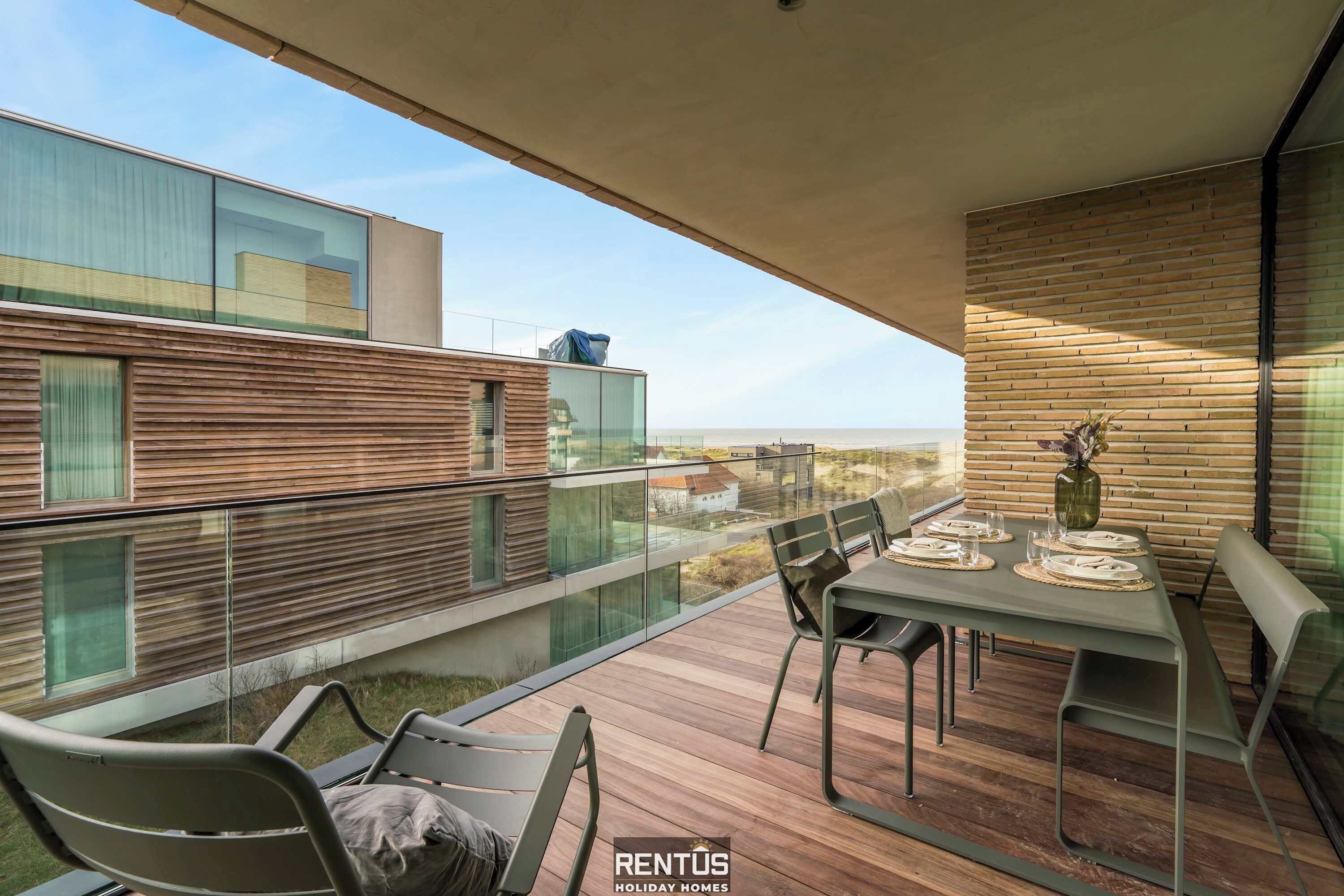 A modern balcony with a dining table set for two, overlooking a scenic view.