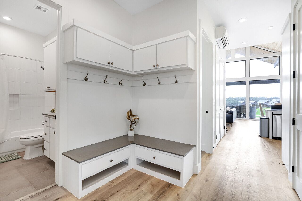 A modern bathroom with white cabinetry, a bench, and a view to the outside.