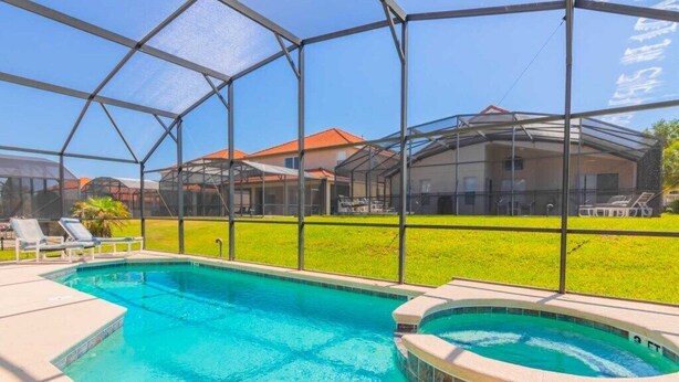 A swimming pool with a glass enclosure, surrounded by a grassy area and houses in the background. - New! Lesa's Disney Vacation Home (Davenport)