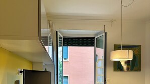 Een moderne woonkamer met een flatscreen televisie, een eettafel met stoelen, een lamp en uitzicht op het buitenbalkon.