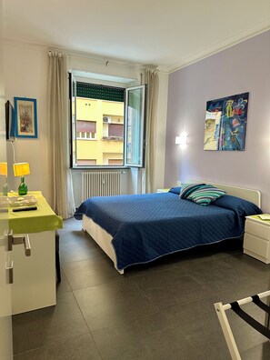 A bedroom with a bed, bedside table, lamp, and a window with curtains. - Scent of Sorrento in Rome  (Roma)