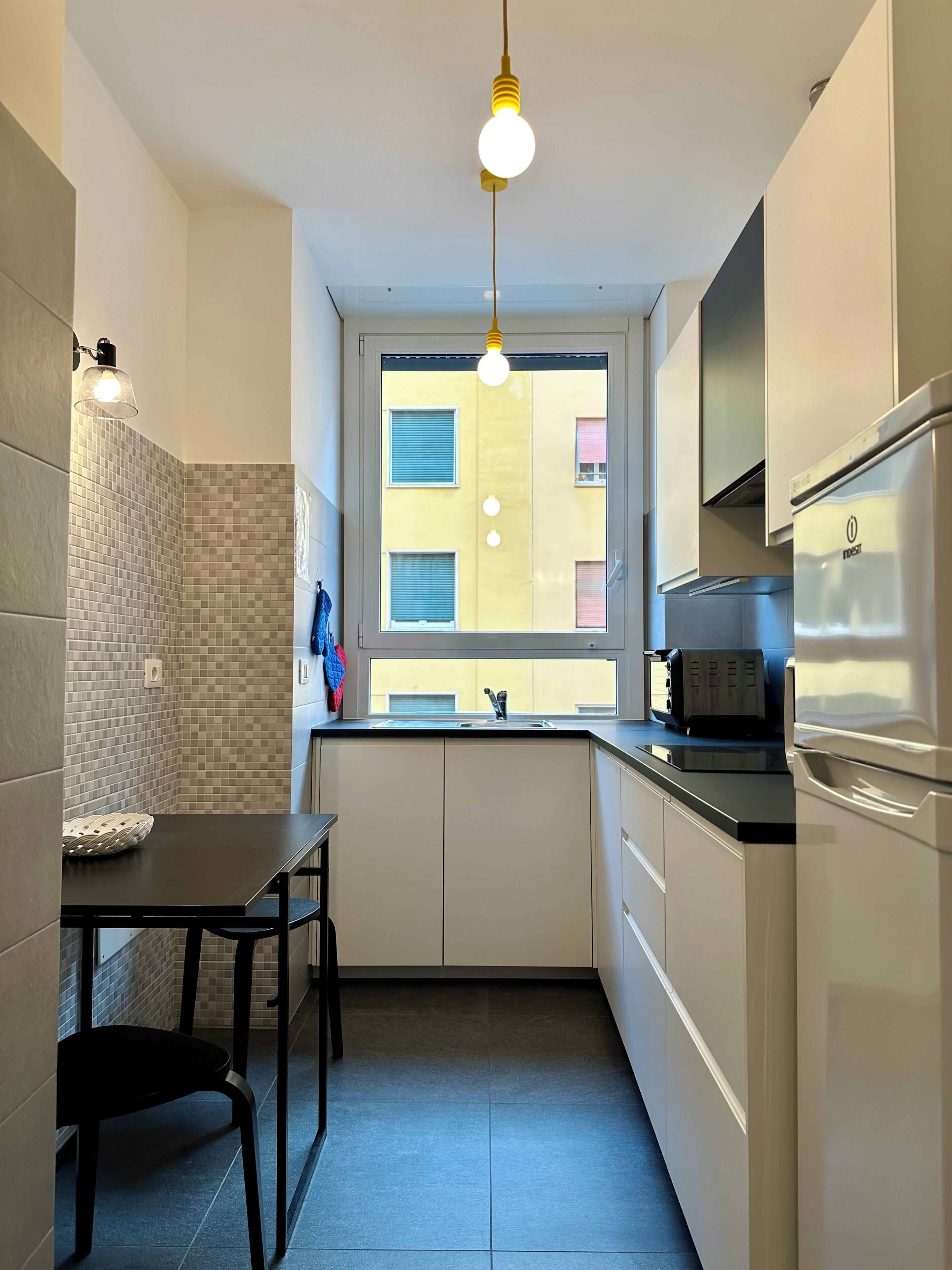 Una cucina compatta con una finestra, una lampada a sospensione, un tostapane e un frigorifero.